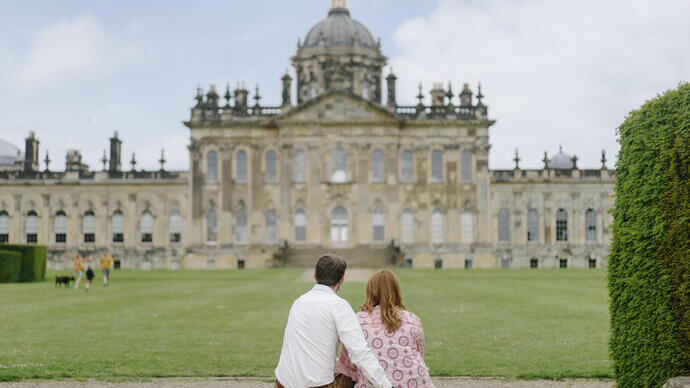 A man and a woman sit on a step looking towards a heritage building