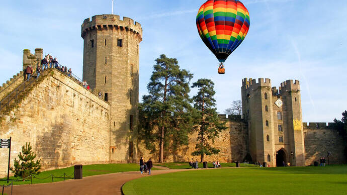 Une montgolfière flotte au-dessus d'un château et de ses jardins soigneusement entretenus.