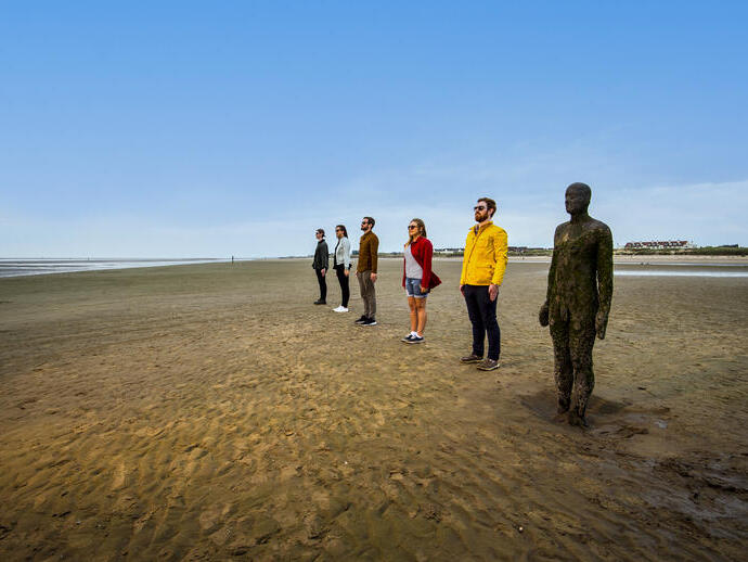 Persone in fila accanto a una statua sulla spiaggia