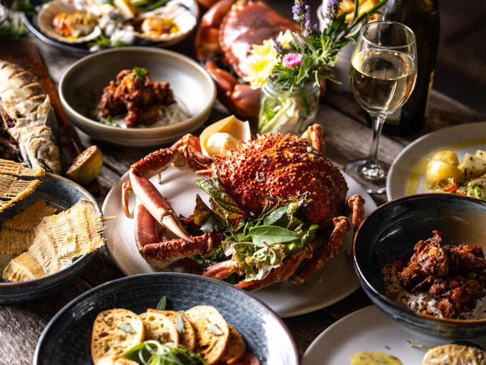 A table with a variety of seafood dishes including crab, fish, scallops, and a glass of white wine.