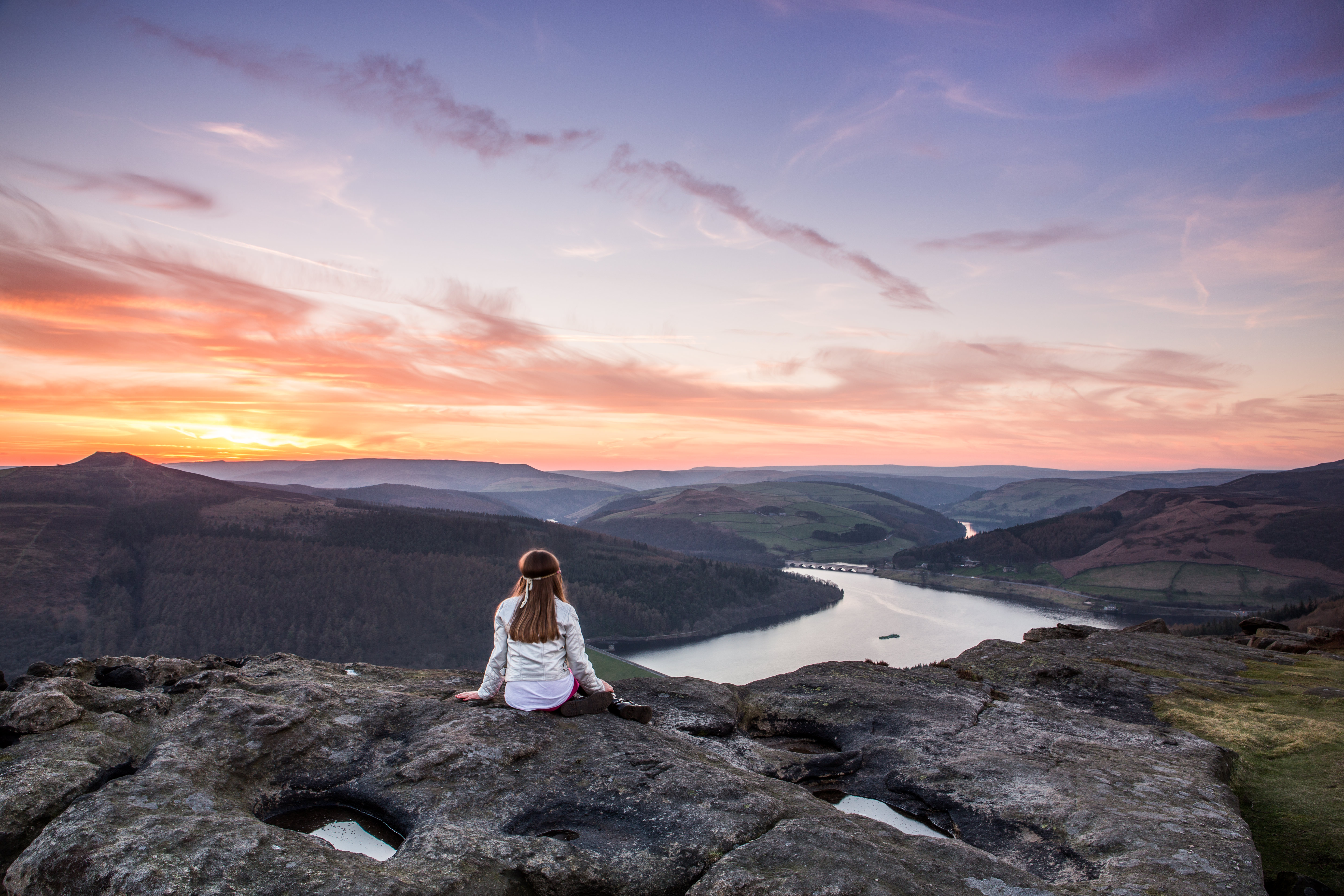 A woman sitting on rocks looking down valley to the river