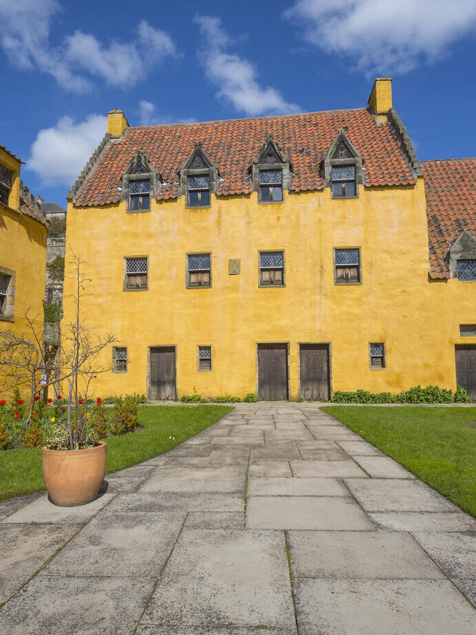 An small, rustic palace painted yellow with red roof tiles and a small lawn on a sunny day.