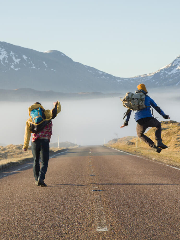 Two men walking and jumping on a road surrounded by mountains