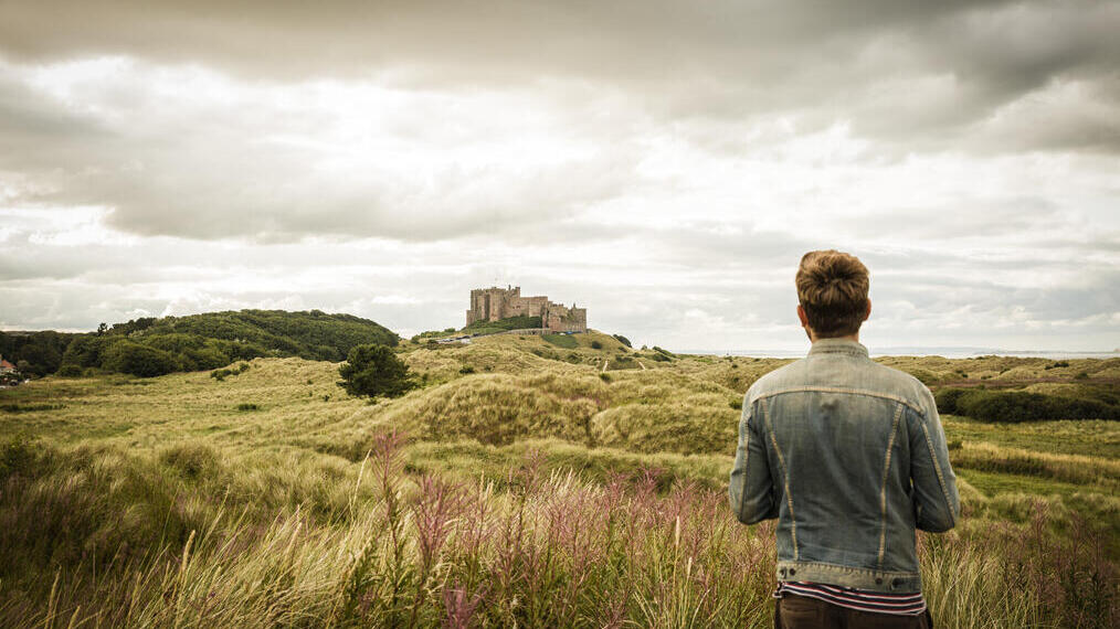 Hombre de pie entre las dunas mirando un castillo