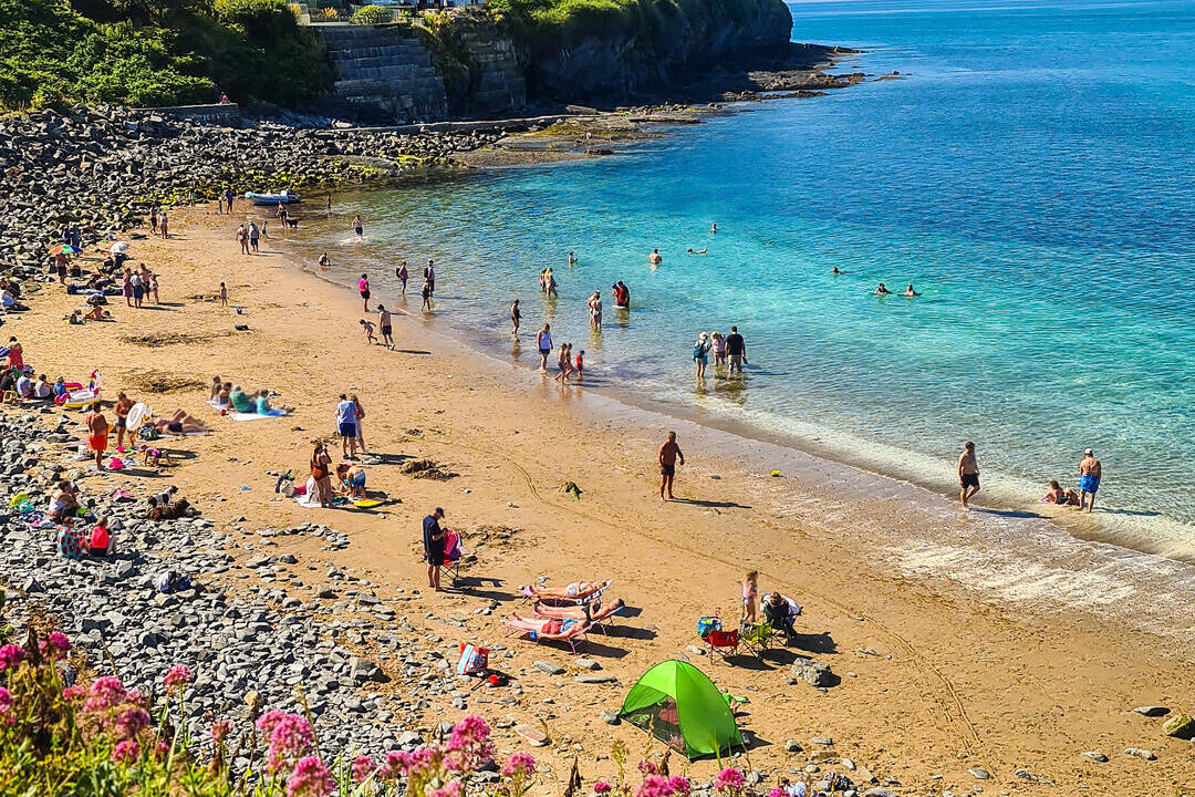 People on a sandy beach in a cove with houses on the cliff behind