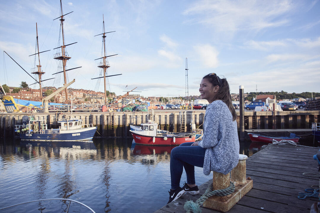 Smiling woman sitting on a jetty in a harbour 