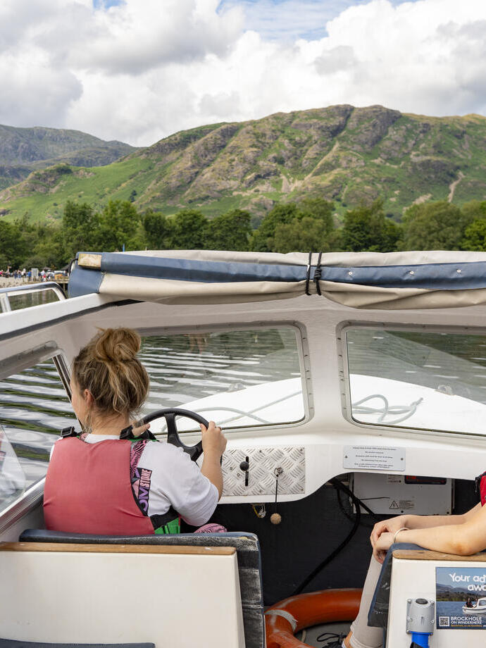 Town women sit ar the front of a boat on a lake with hills beyond
