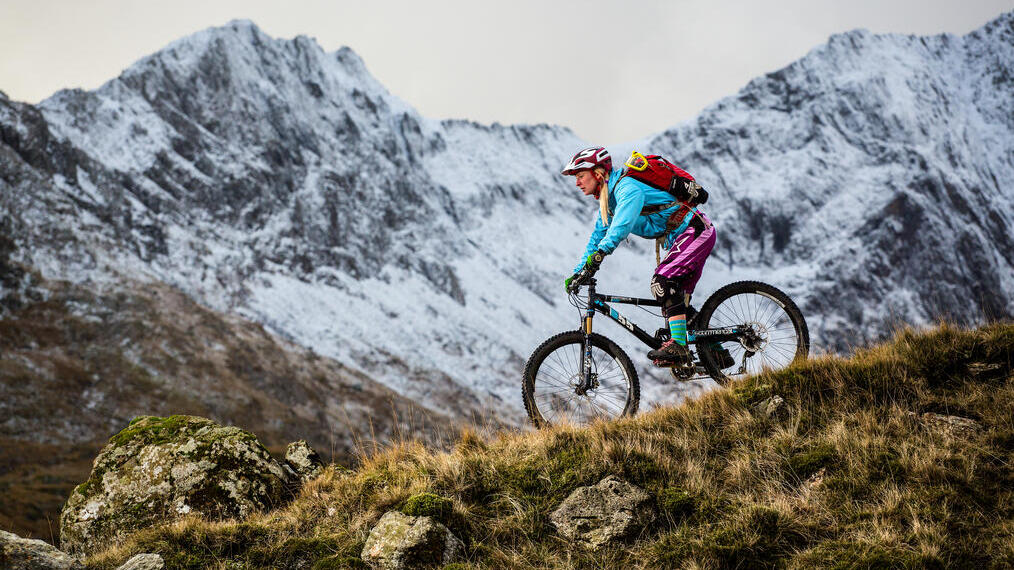 Mountain biker rolling down a slope. Mountain backdrop