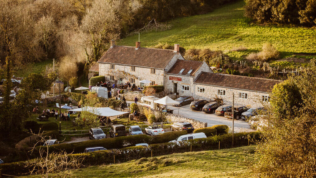 Rural view of a pub from an elevated position looking across fields to the pub in the background.