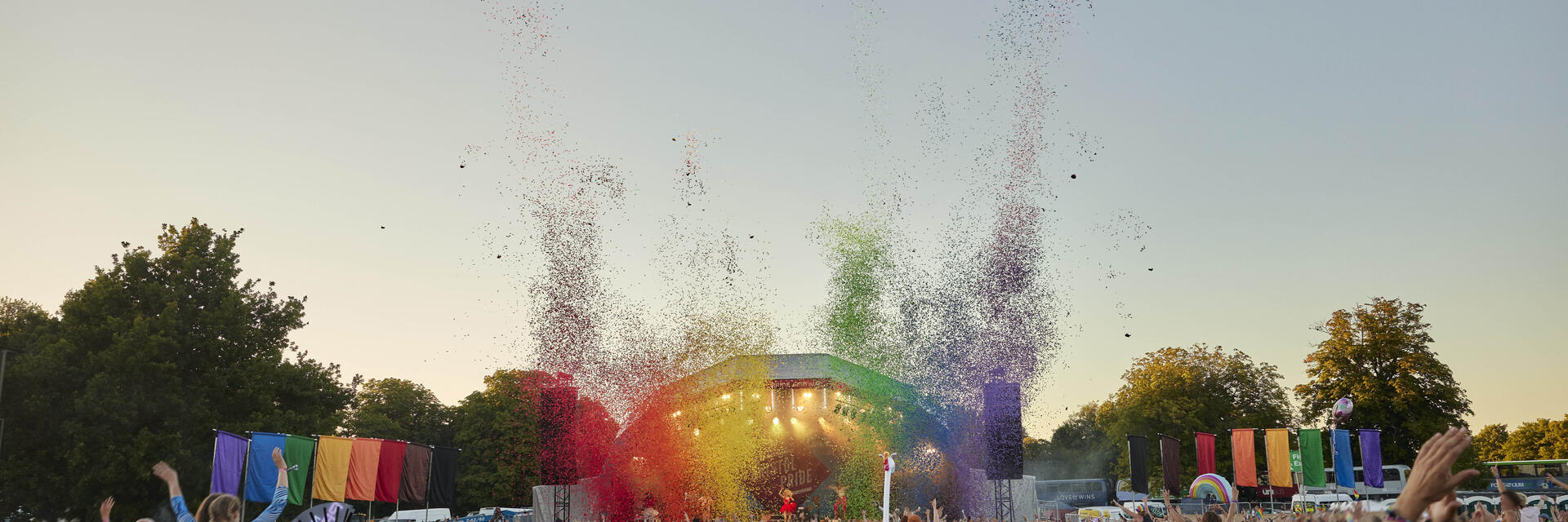 Vista trasera del público en el evento, con el escenario decorado con los colores del arcoíris