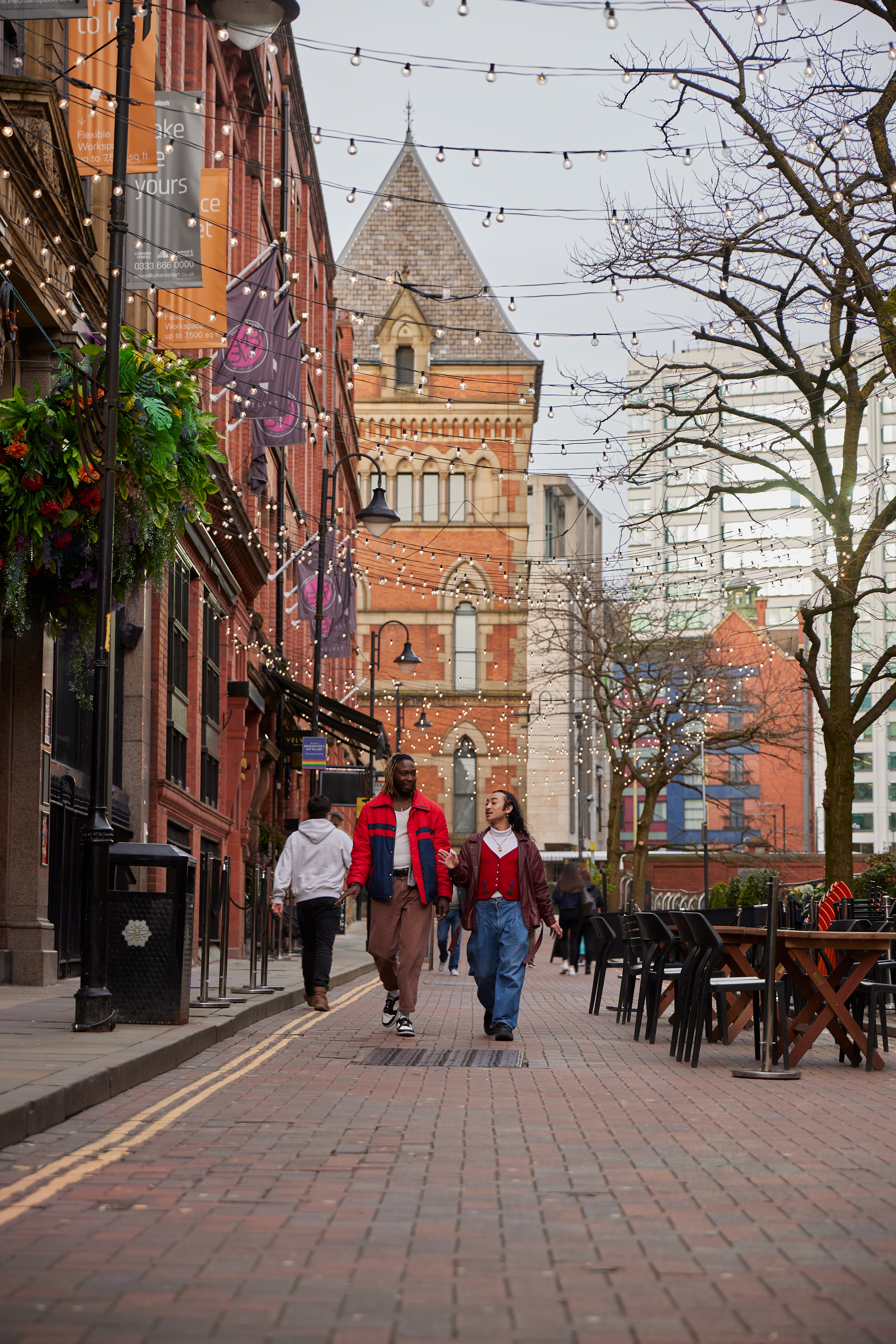 Two men chatting and walking down a street with cafes and a canal.