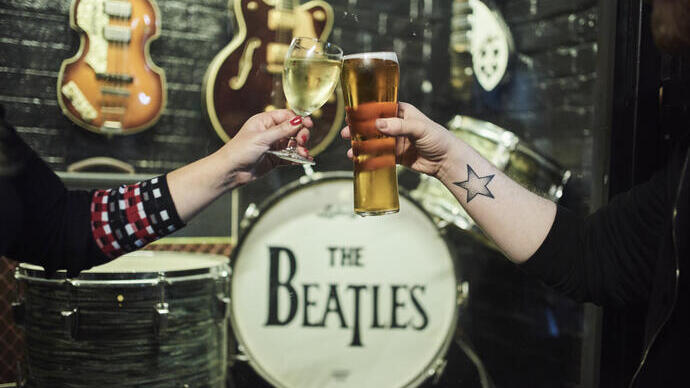 Two people clinking glasses in front of a drum kit and guitars
