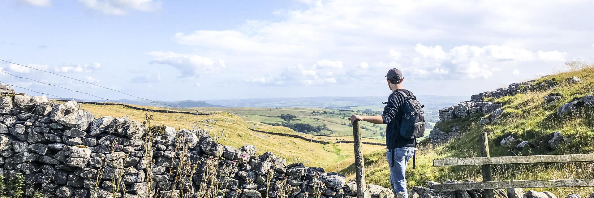 Man standing on stile over stone wall looking at landscape