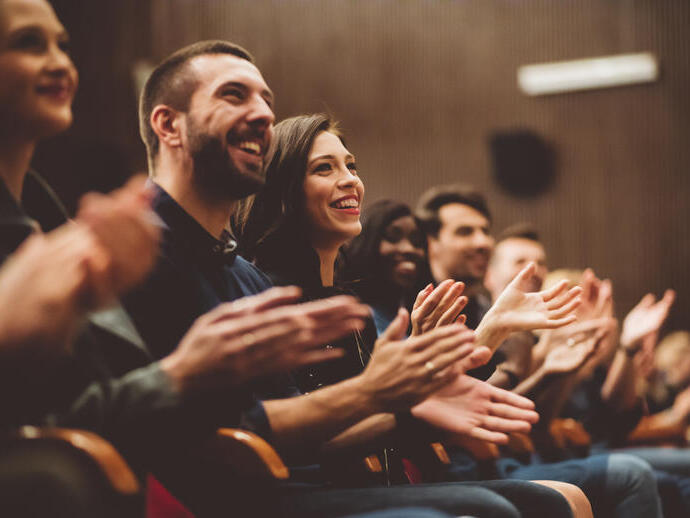 Grupo de personas sonrientes aplaudiendo en el público del teatro.