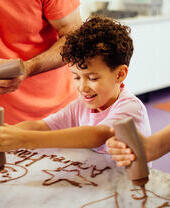 A boy, with curly hair, squeezing chocolate out of a bottle