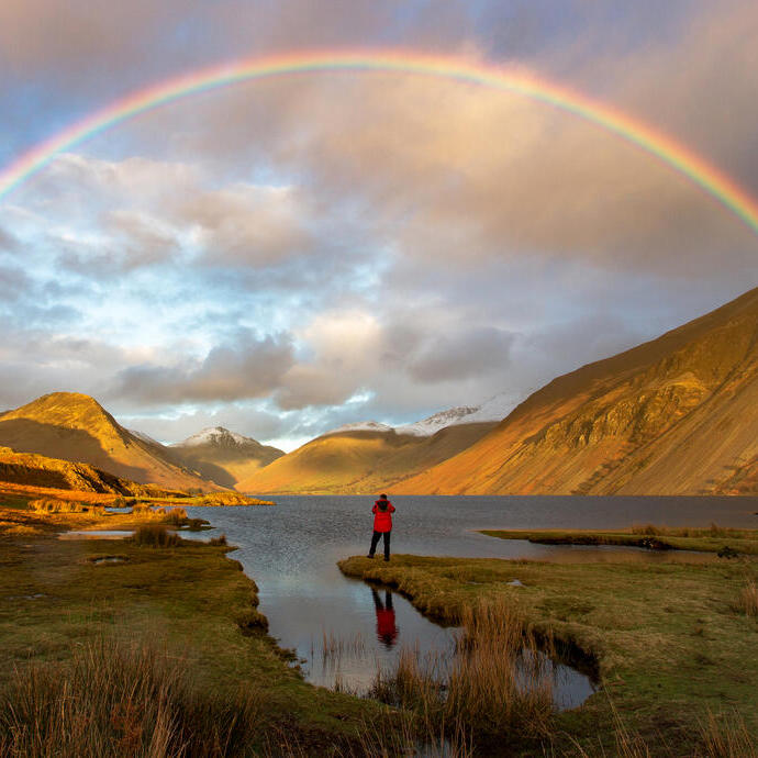 Man standing on the edge of a lake watching a rainbow