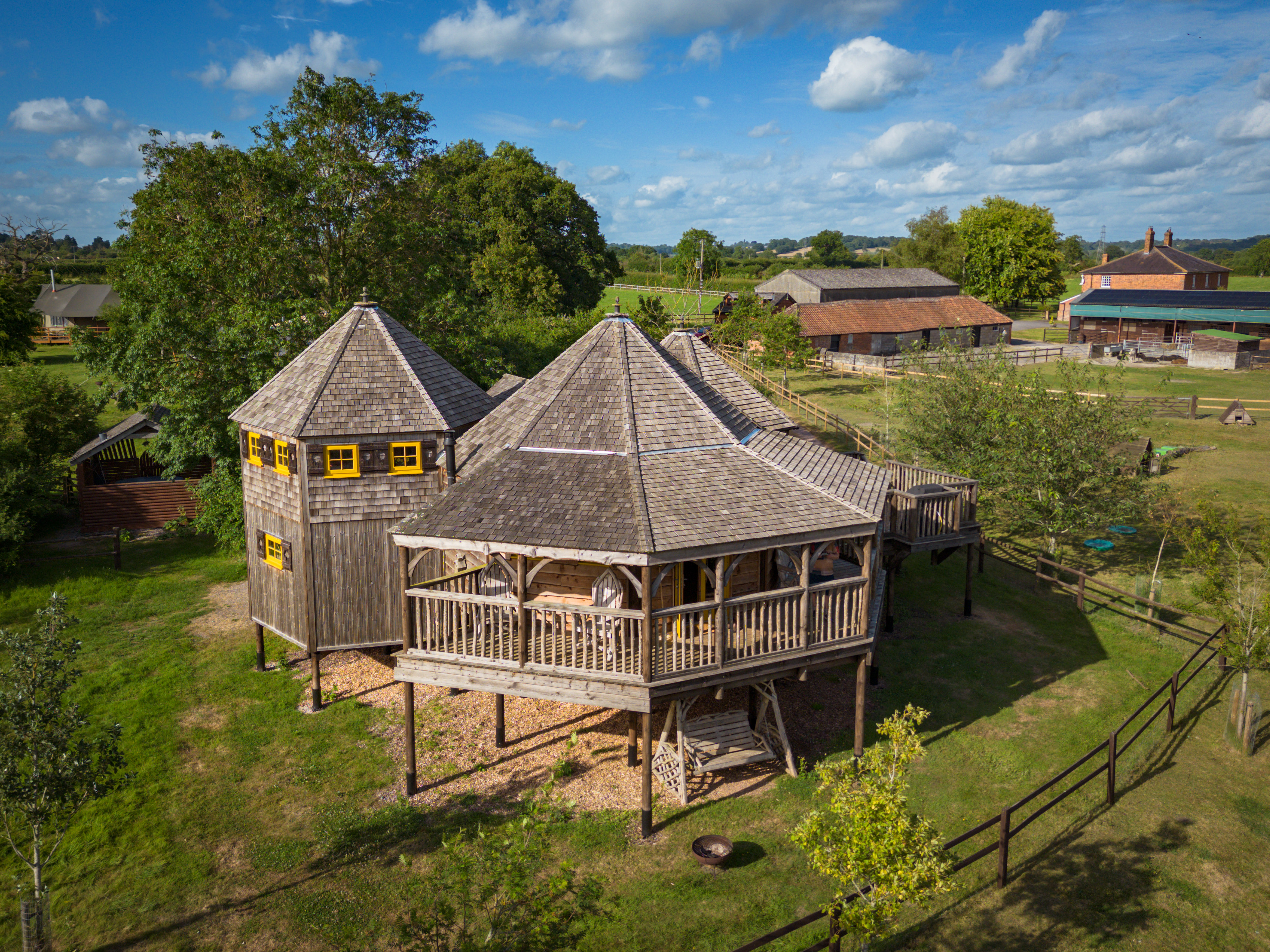 The exterior of a large two-storey wooden treehouse-style lodging in a field .