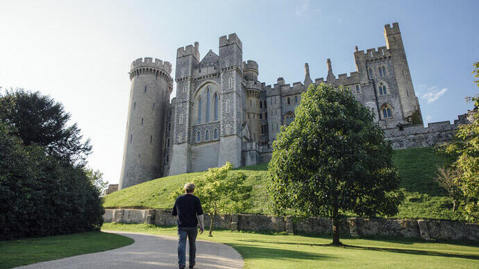 Man walking on a path towards a large medieval castle.