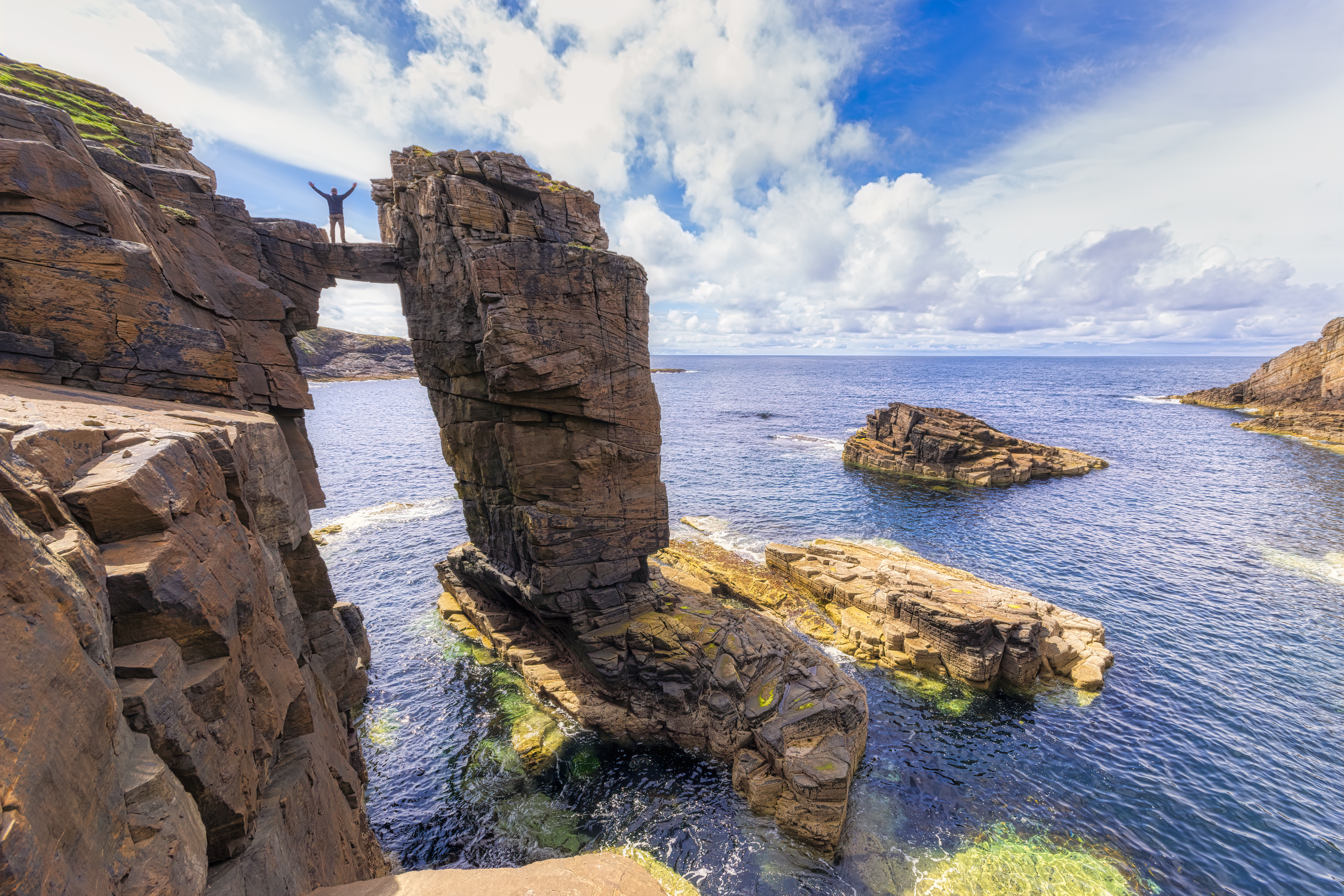 Man straddling two sea stacks overlooking a rocky outcrop and the ocean