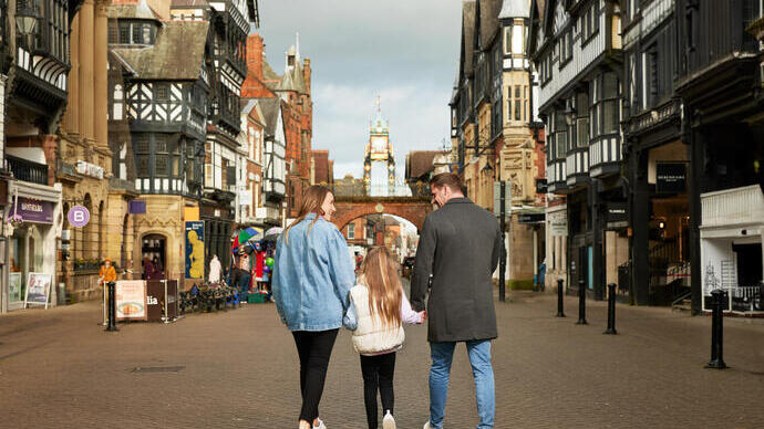 A family of three in front of a town square clock tower in a shopping precint.