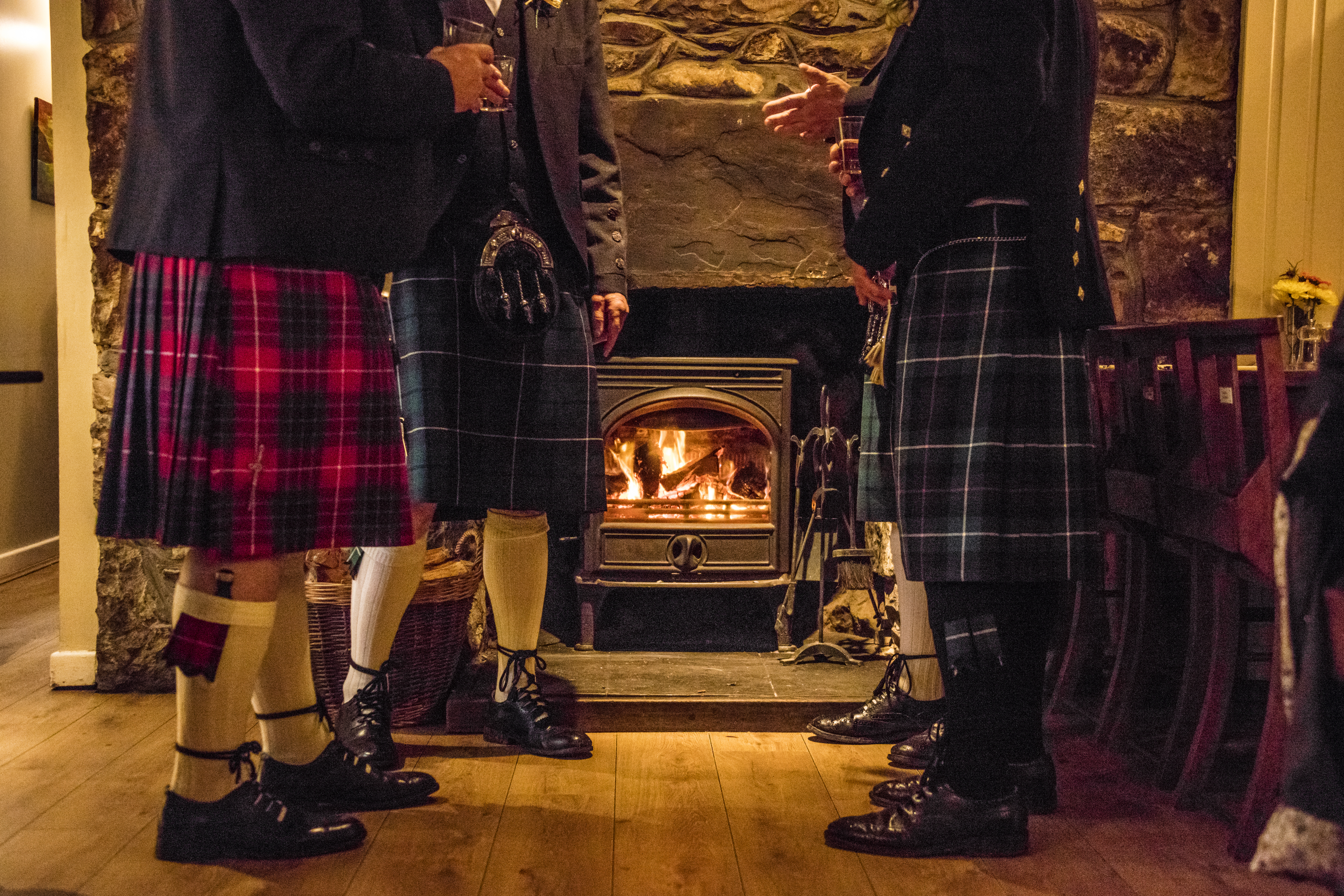 Männer in Kilts, die an einem Kamin in einer Kneipe stehen und trinken