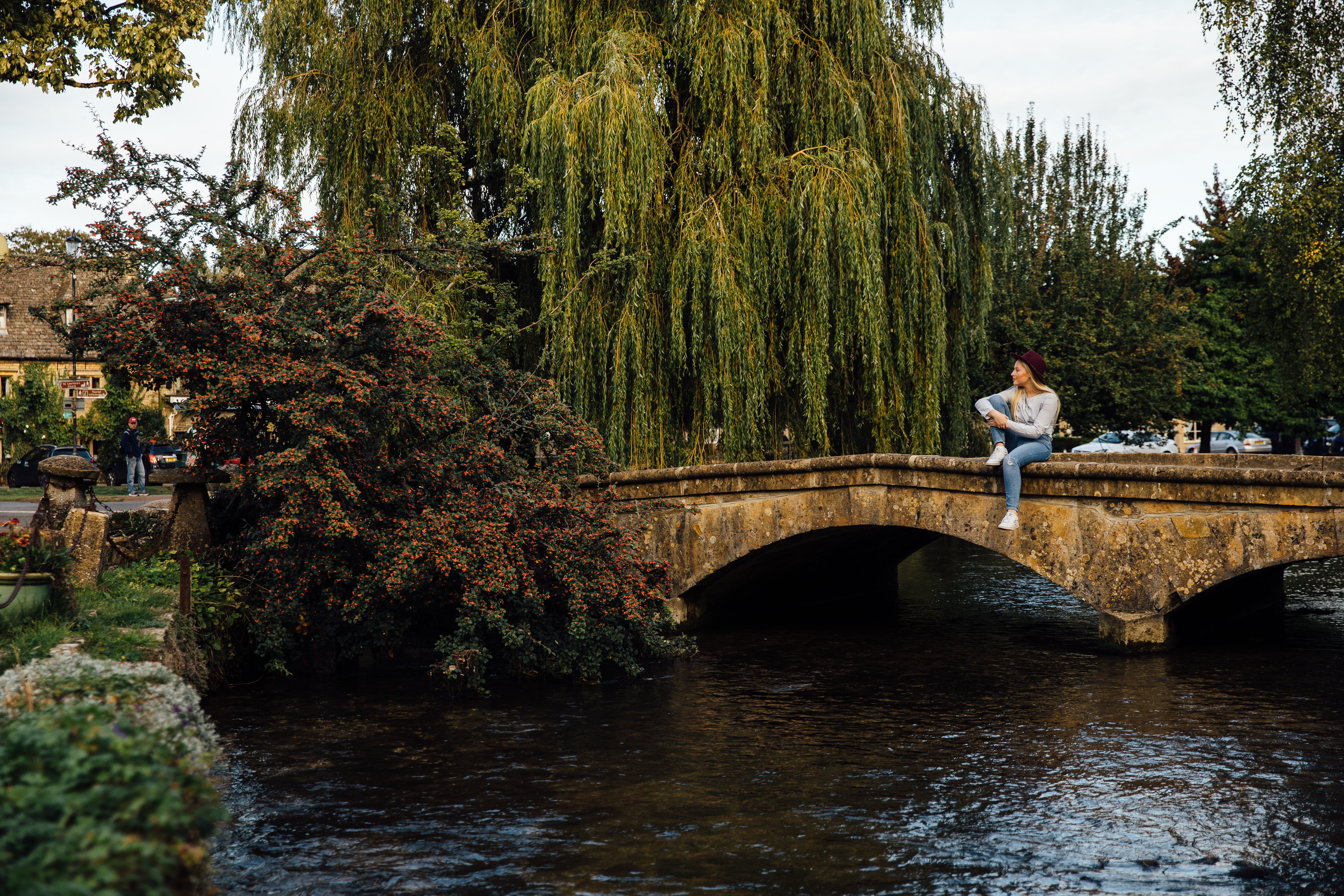 Woman sitting on a low stone bridge over a river in a village