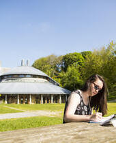 A person sitting at a bench writing outside Aberystwyth Arts Centre