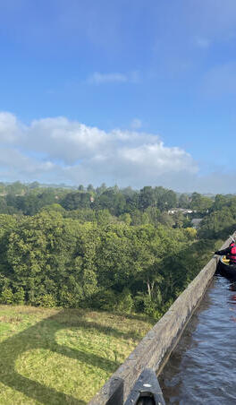 A group paddling kayaks across a viaduct with scenic views of Snowdonia/Eryri National Park