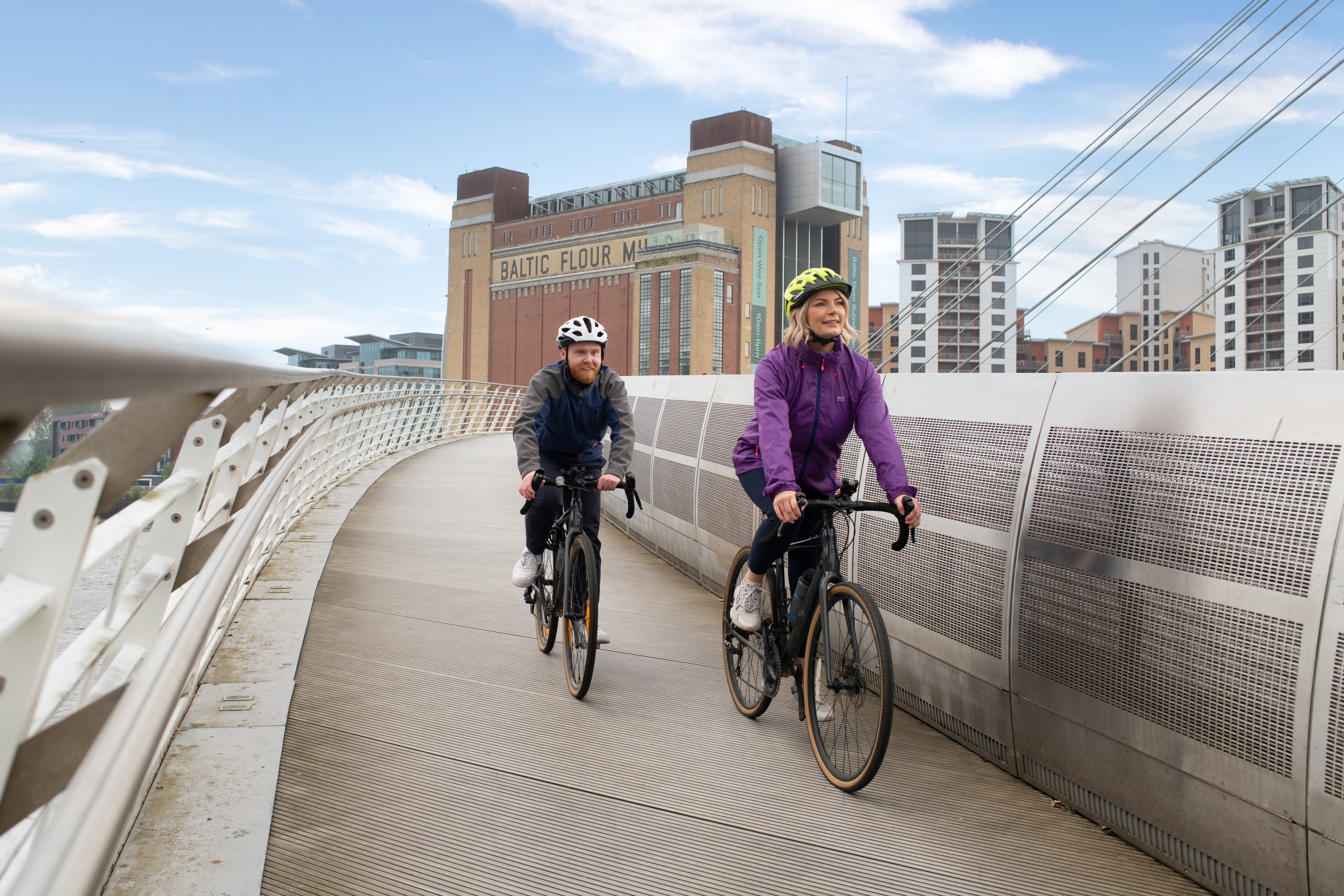 A man and a woman cycle over a bridge in front of an iconic building
