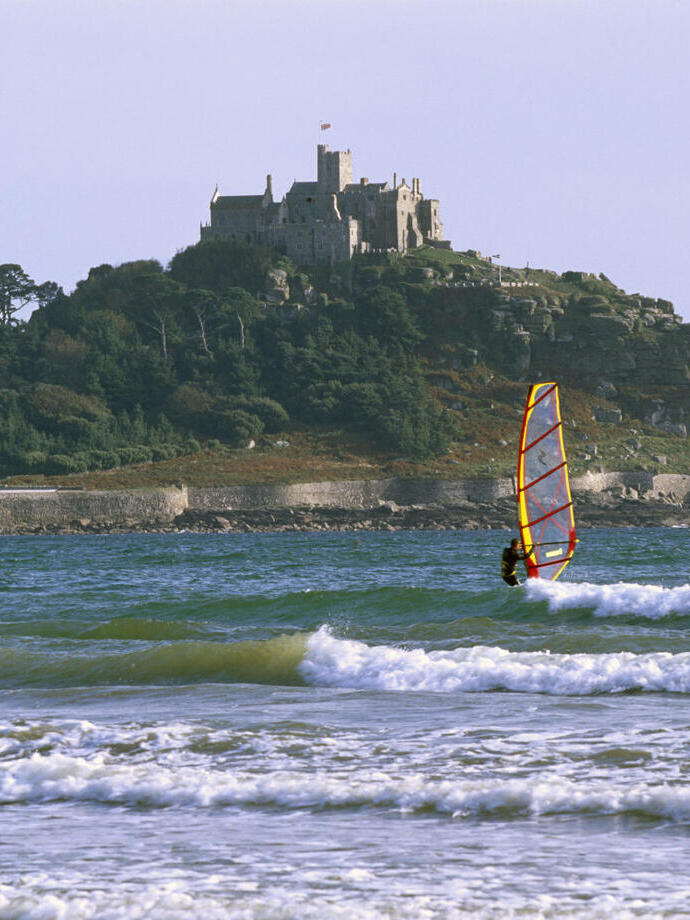 A person windsurfing off the coast of the castle on St Michael's Mount, Cornwall