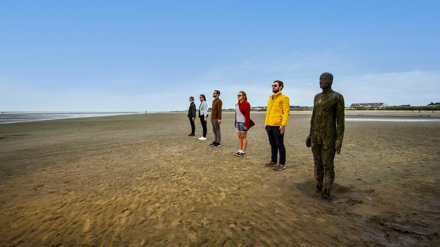 People standing in line beside a statue on the beach