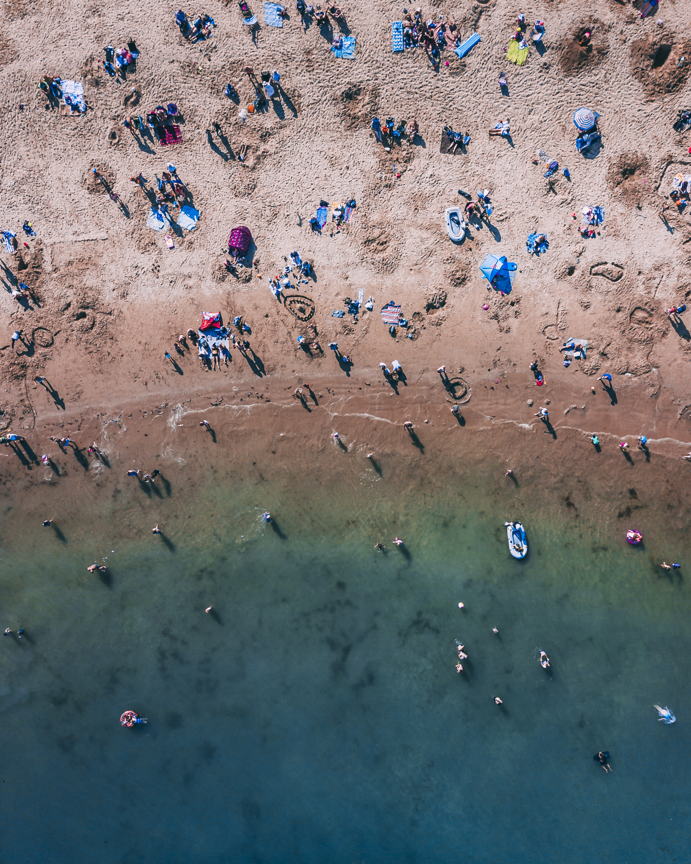 Aerial view of people on sandy beach and swimming in sea