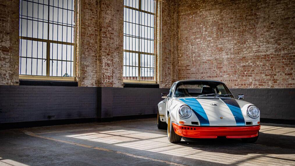 Classic race car with blue stripes and red bumper in an industrial space with brick walls and large windows.