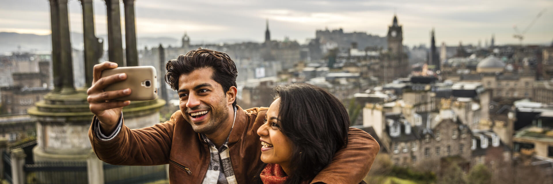 زوجان يلتقطان صورة سيلفي بهاتف محمول مع مدينة في الخلفية