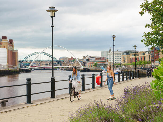 Two people cycling and skateboarding on a path along the River Tyne in Newcastle.