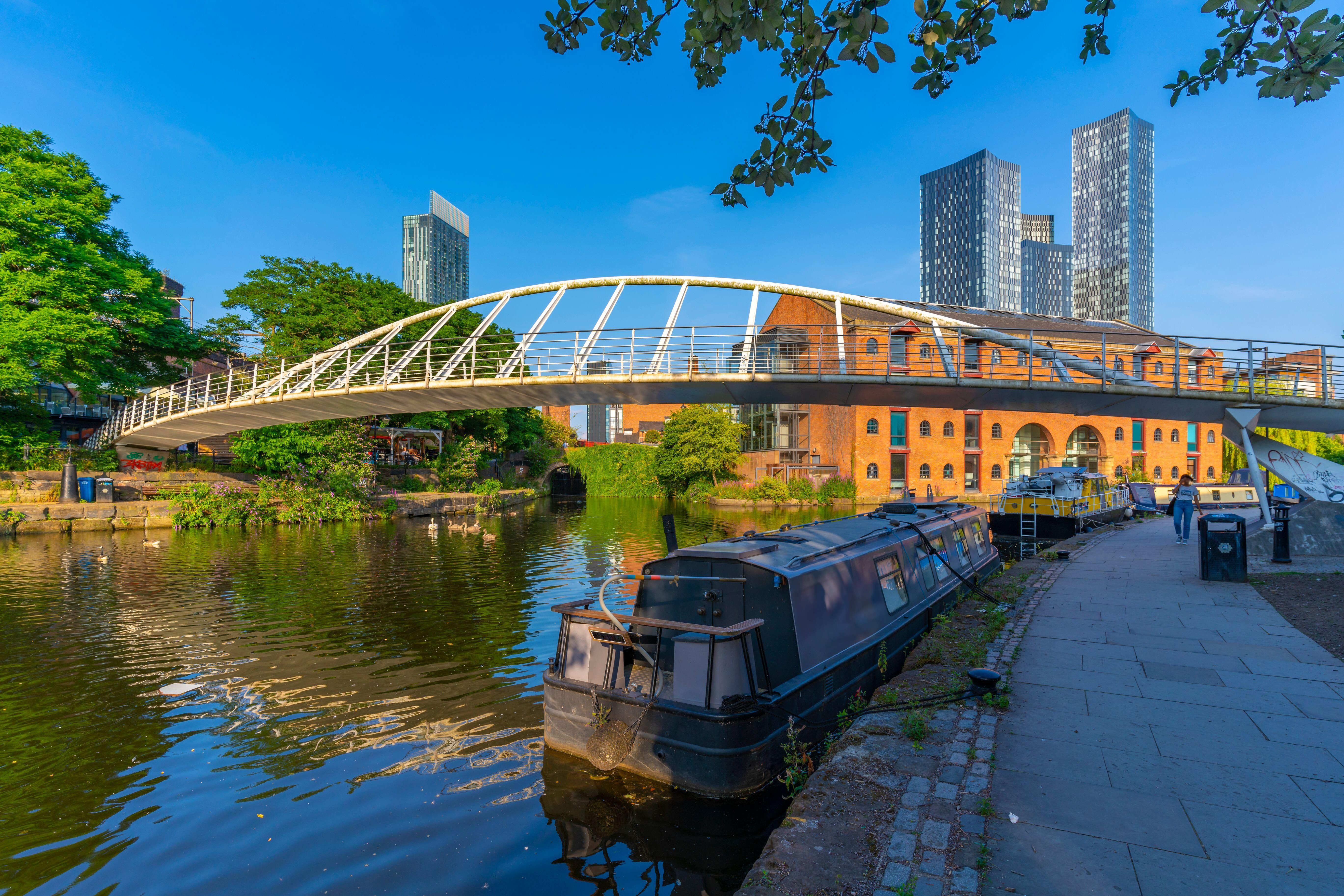Barco amarrado en un canal con un puente peatonal y edificios de la ciudad al fondo