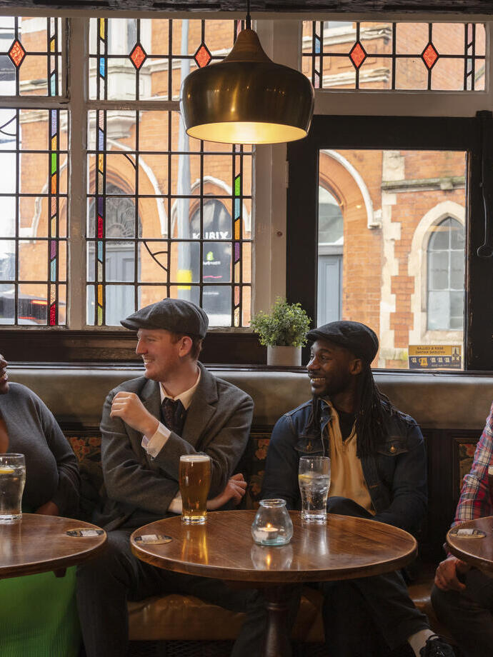 Cuatro amigos sentados en una mesa junto a la ventana de un pub tomando una copa
