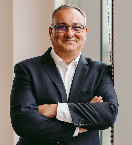 A person in a suit standing with arms crossed near a window.