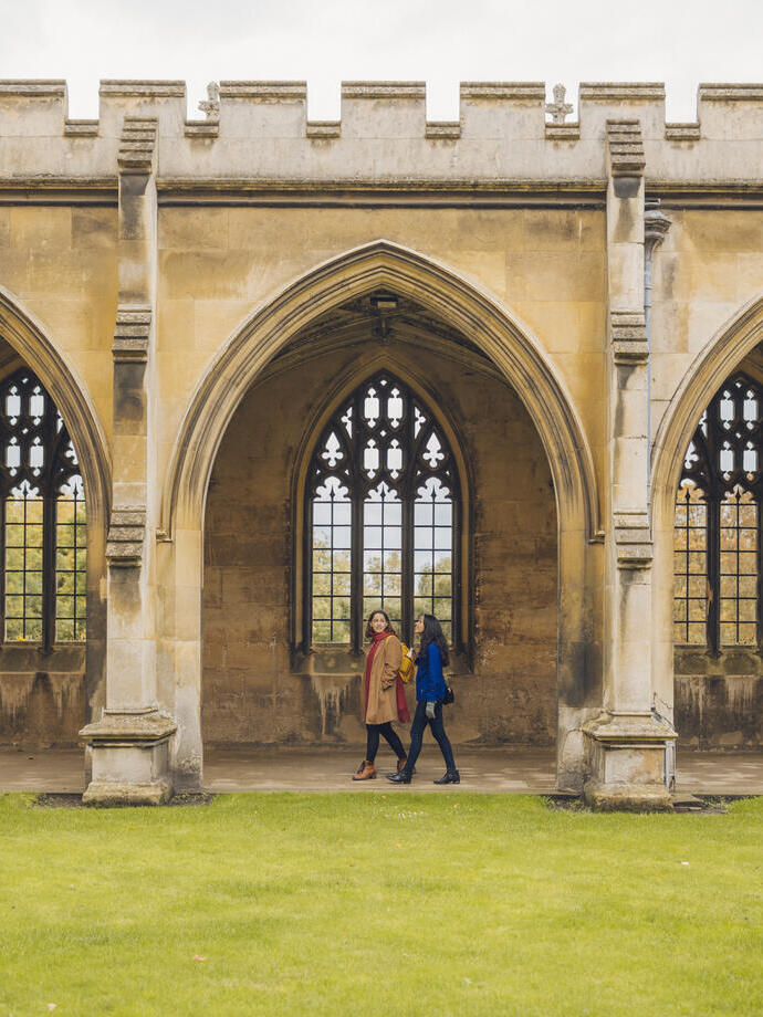 Two women walking under the arches of a college quad