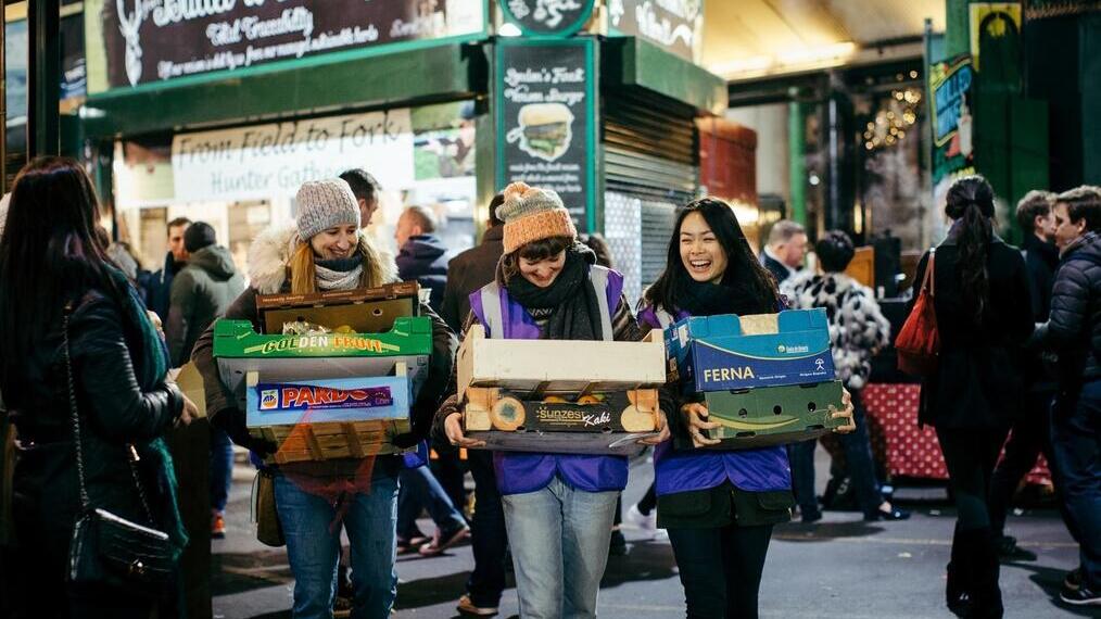 Three women carrying small crates containing fruit and vegetables at Borough Market