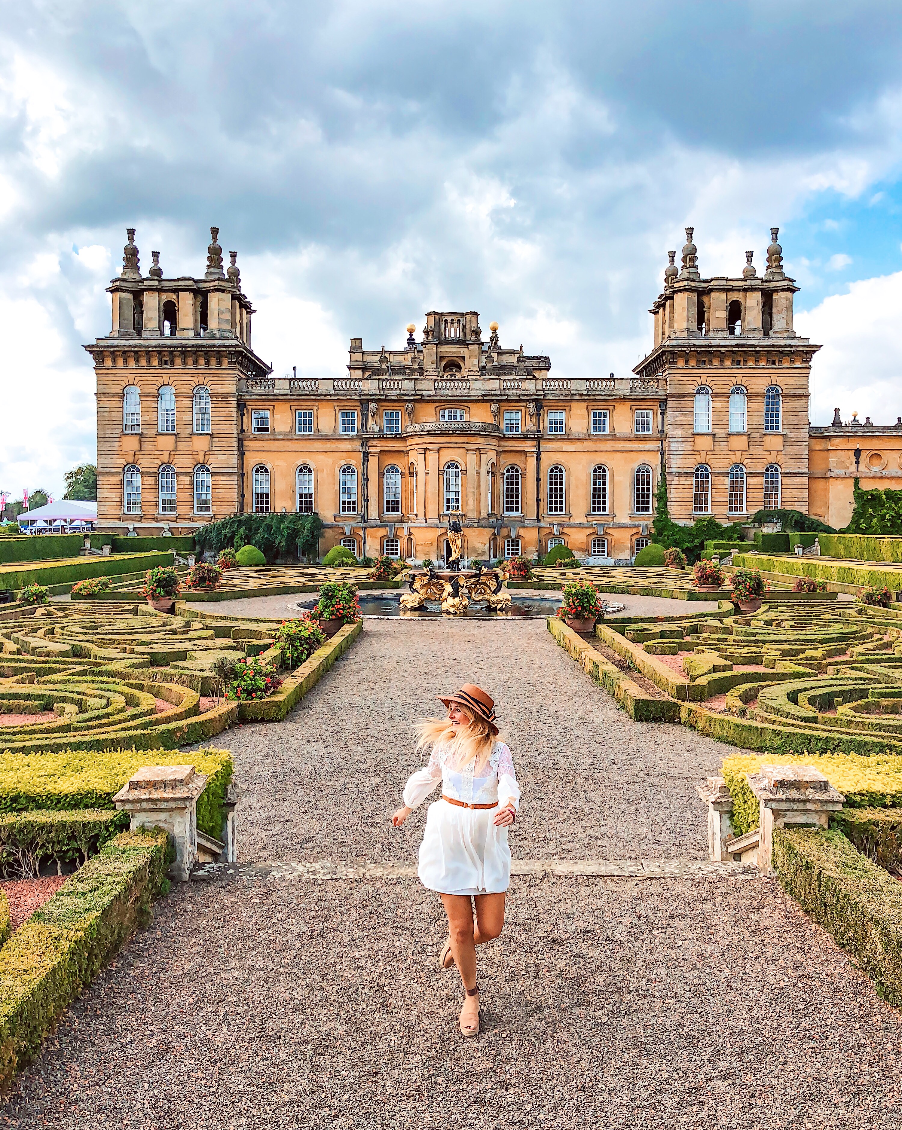 Mujer caminando por los jardines formales frente a un palacio
