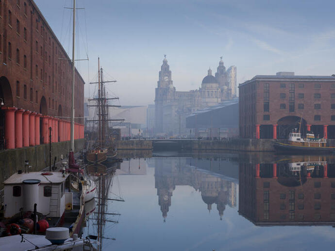 Dock with wooden ship and tall buildings on skyline.