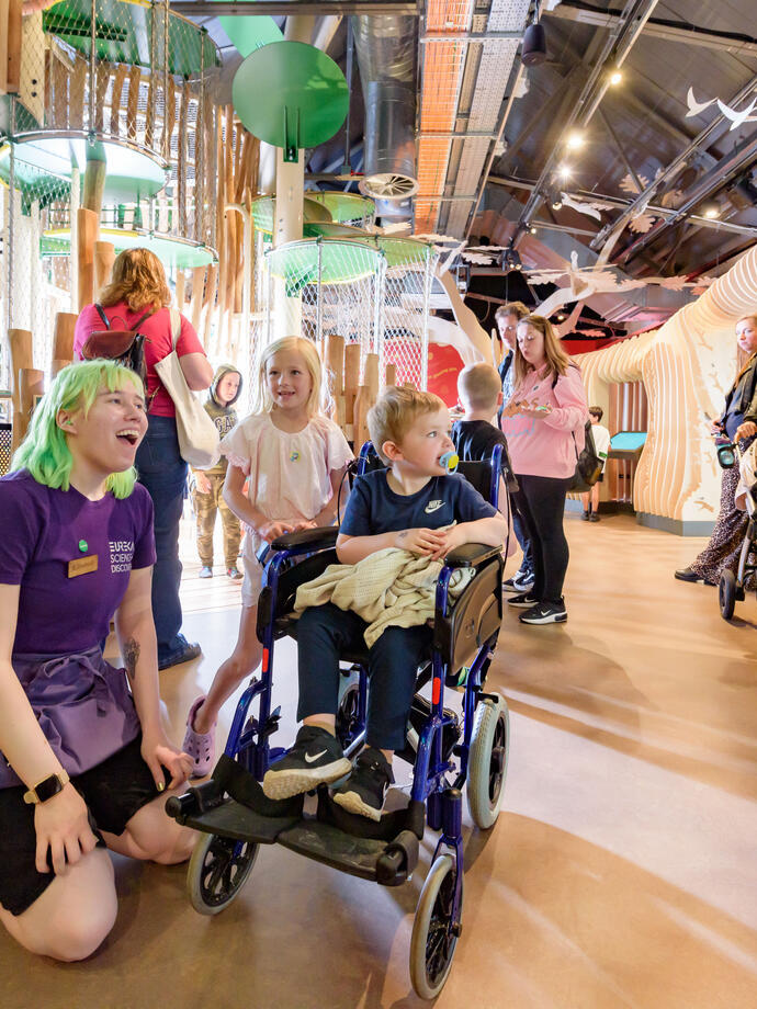 Inside a Science & Discovery Centre with children, including one wheelchair user and staff member. 