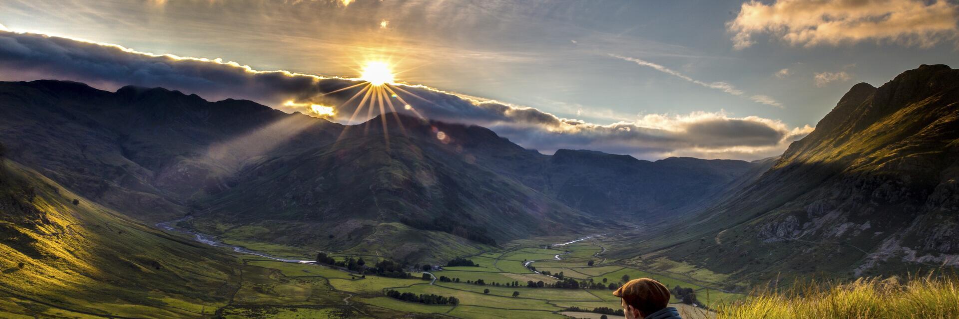 Mann, der im hohen Gras am Rande eines Hügels sitzt und den Sonnenuntergang beobachtet