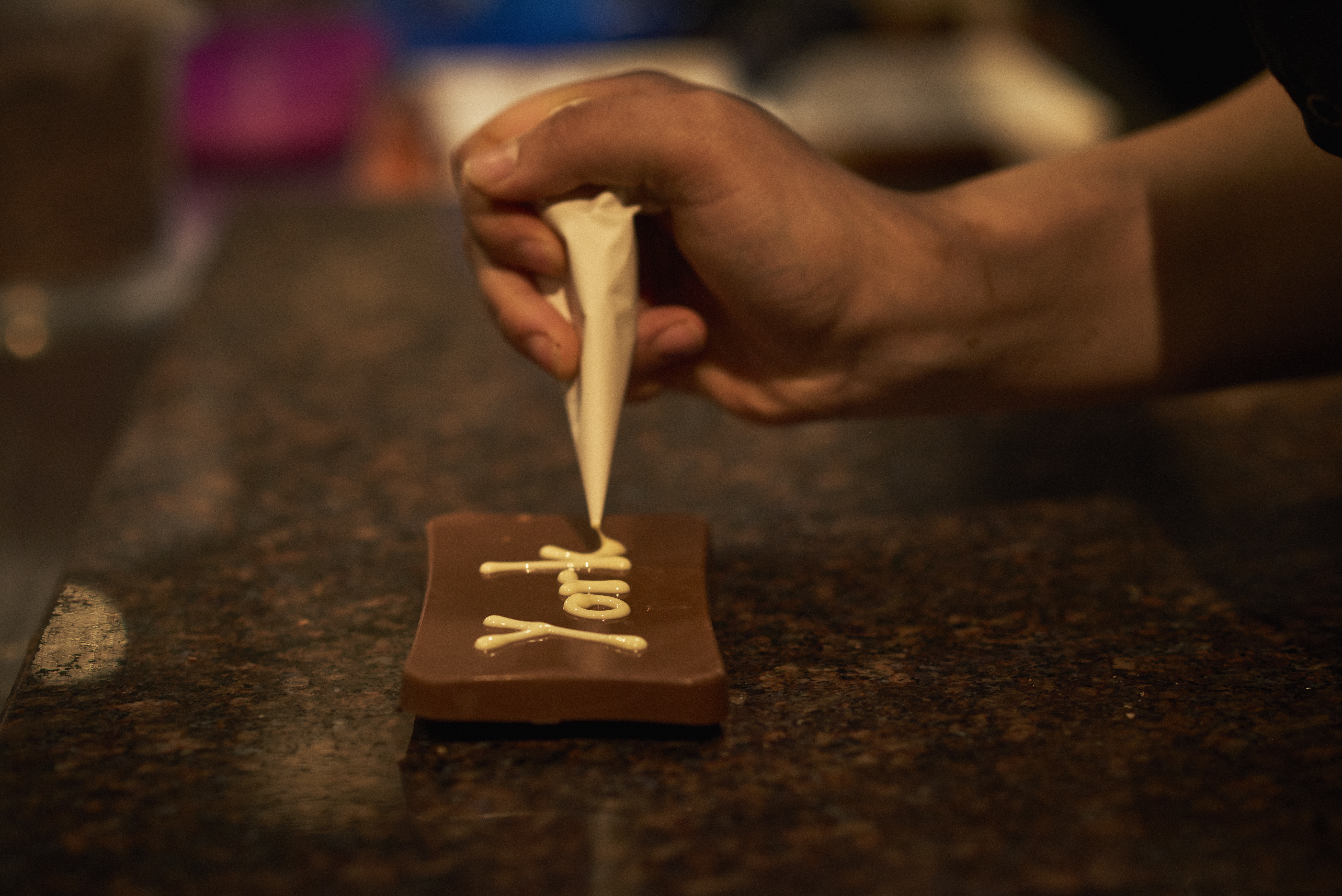 Person decorating dark chocolate with white chocolate piping