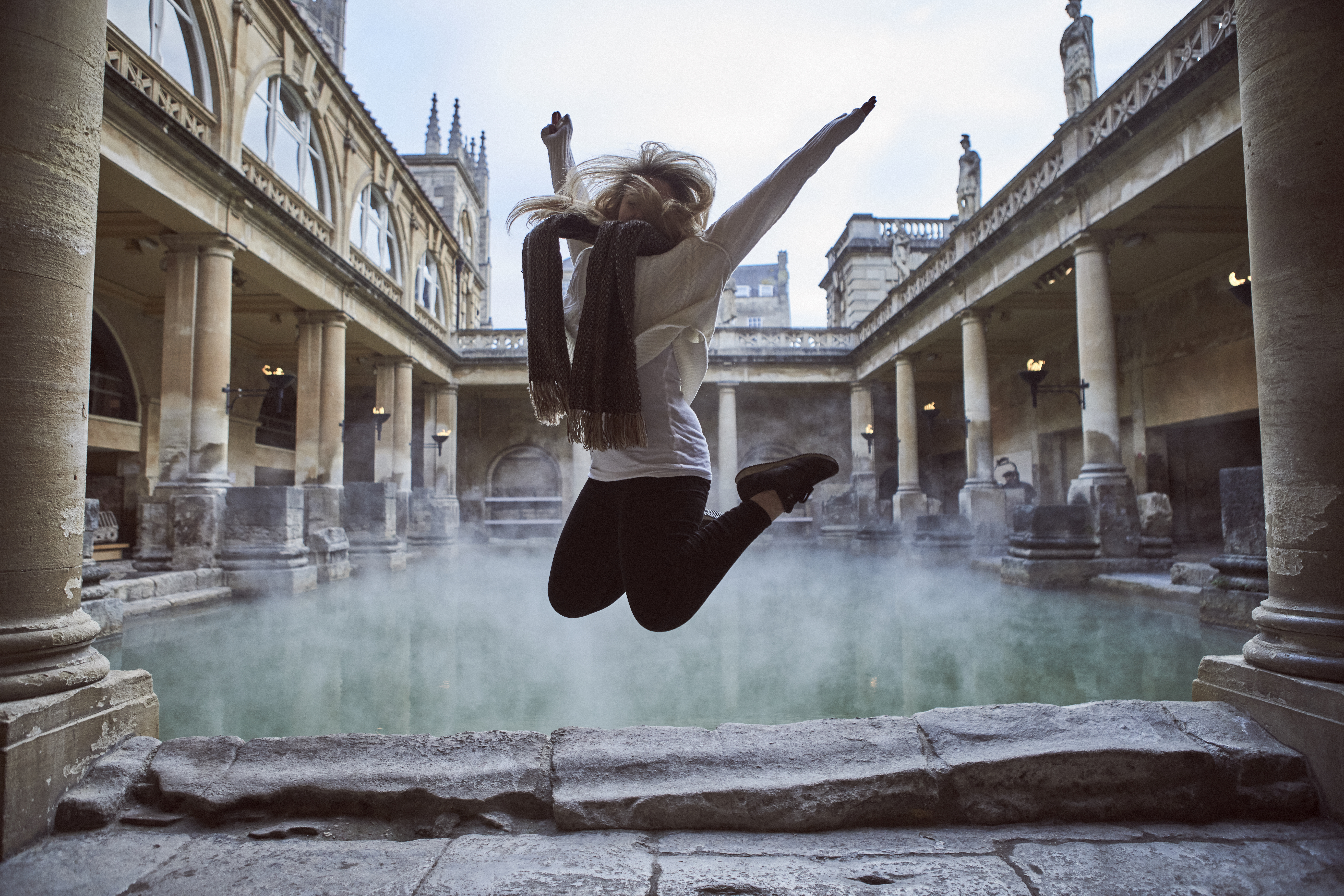 Woman leaping in the air at The Roman Baths, Bath, Somerset, England.