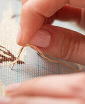 Close-up of hands doing embroidery with a needle and thread on fabric featuring a partially completed pattern.