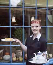 Member of restaurant staff holding a tray with tea and a cake on a plate