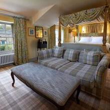 Bedroom at the Devonshire Arms at Pilsley, Derbyshire with a grey tartan upholstered sofa and large foot stool in the foreground, matching tartan carpet and floral curtains and matching draped four-poster bed in the background.