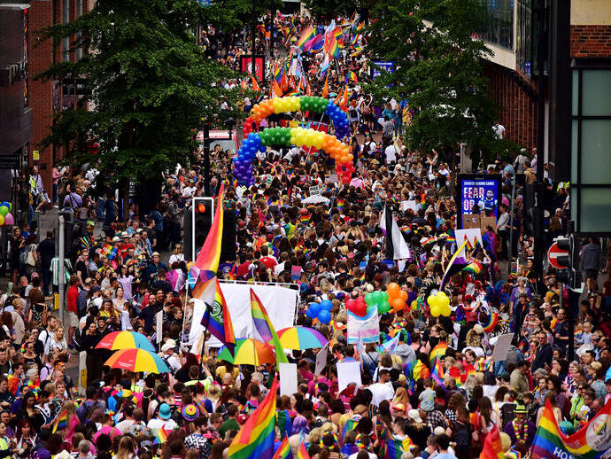 Crowd marching at a parade, holding rainbow flags, umbrellas and balloons